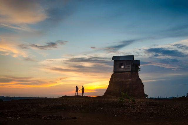 Couple Holding Hands Silhouetted Against Stunning Sunset, Building on Elevated Landform - Download Free Stock Images Pikwizard.com