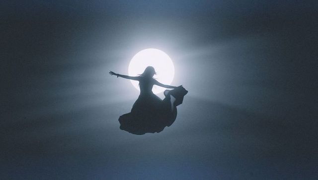 Silhouette of Woman Soaring Against Luminous Full Moon