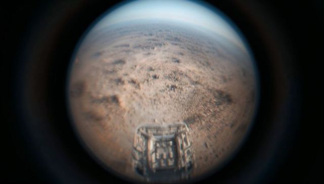 Capturing fisheye rover deck over dusty red plain with curved horizon and extraterrestrial landscape