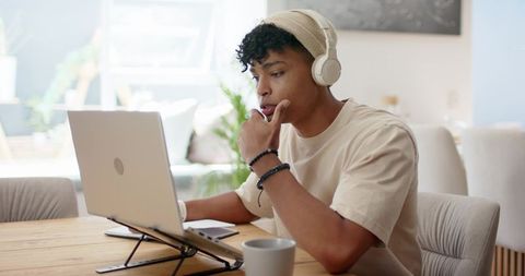 Young african american man working from home on laptop stand wearing headphones and beanie