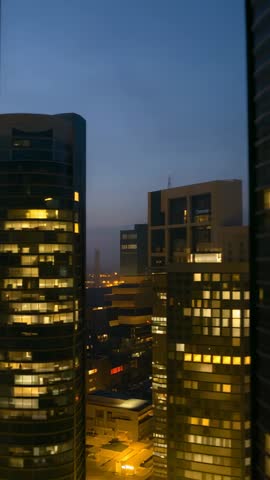 Vertical twilight city video showing glowing skyscraper windows and busy urban nightscape