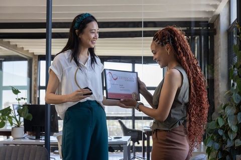 Diverse female coworkers celebrating achievement with certificate exchange