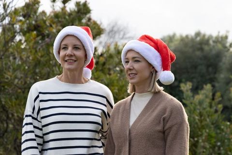 Middle-aged women wearing santa hats smiling outdoors in green garden holiday moment