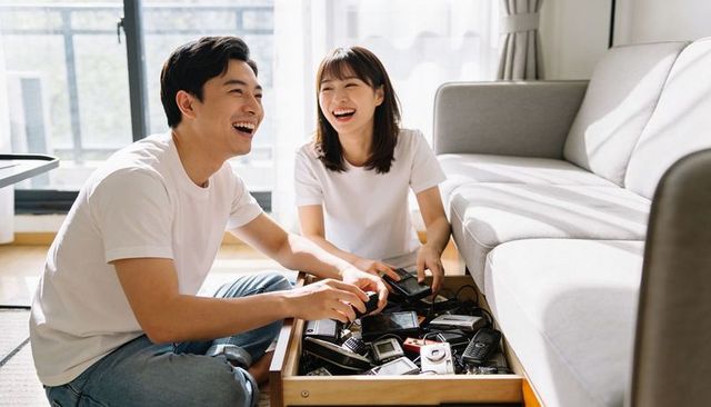 Young couple laughing and sorting vintage mobile phones in sunlit living room