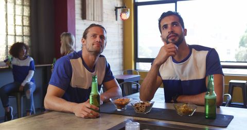 Male friends watching sports game at bar enjoying drinks