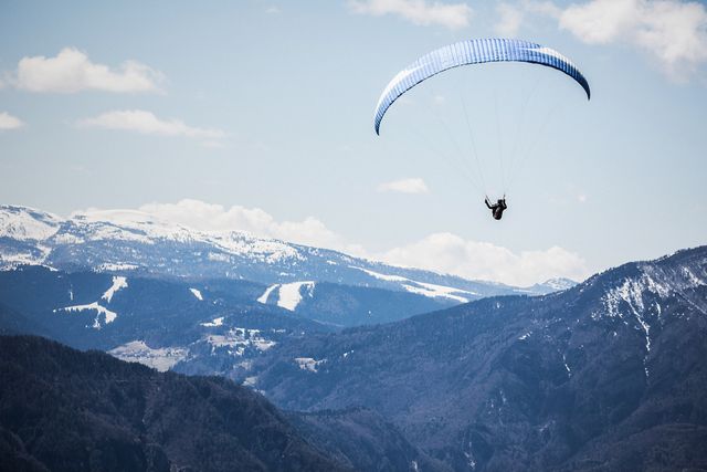 A person paragliding high over a mountain range with snow-capped peaks under a clear sky. This image can be used to represent adventure, extreme sports, outdoor activities, or travel and tourism marketing materials. Ideal for websites, blogs, or promotional content focusing on nature exploration or high adrenaline sports.