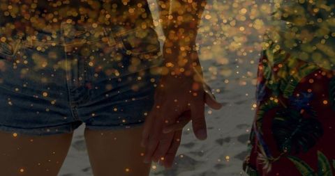 Couple holding hands on sunlit beach with golden bokeh, denim shorts and tropical colors