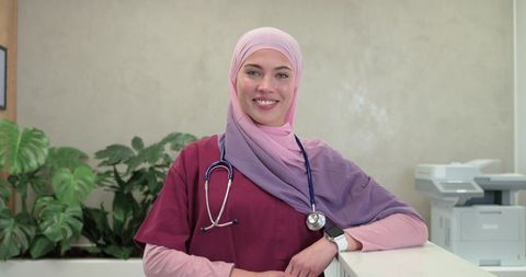 Smiling nurse wearing pastel hijab and stethoscope checking smartwatch at clinic reception