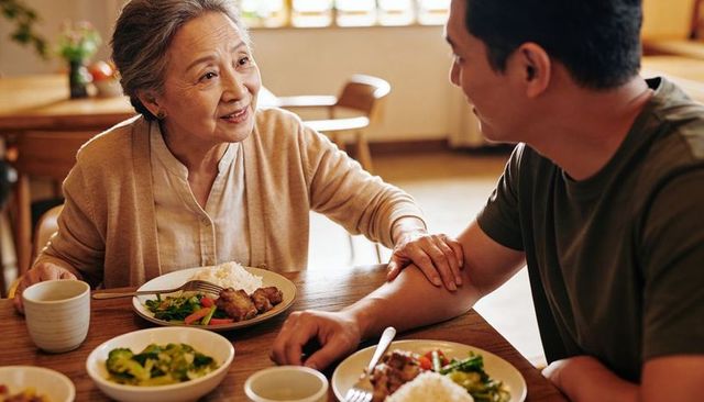 Senior mother gently holding adult son forearm while sharing warm family meal at home