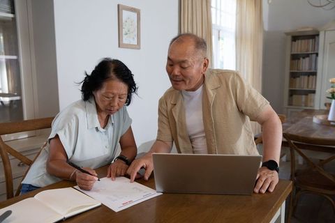 Senior couple collaborating on household finances at home signing documents with laptop