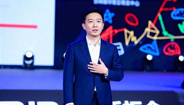 Keynote presenter speaking on stage in navy suit with headset mic and colorful led backdrop