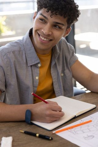 Male student sketching in notebook at sunlit table