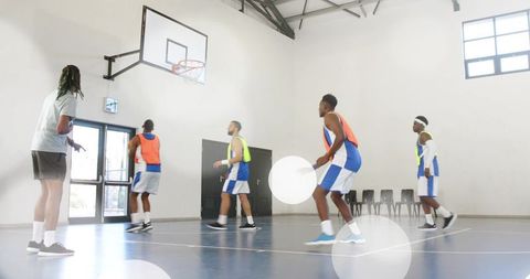 Adult men practicing basketball scrimmage on bright indoor court with coach guiding drill