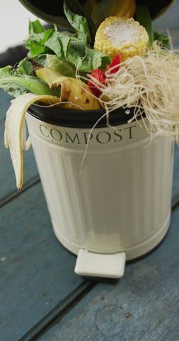 Full compost bin filled with organic waste on wooden surface