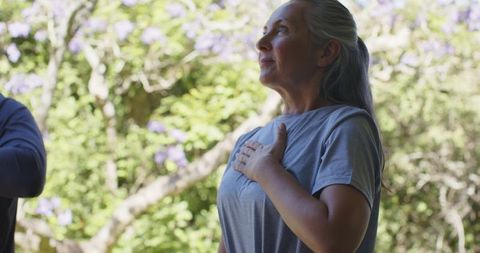 Senior woman placing hand on chest while gazing in garden with purple blooms