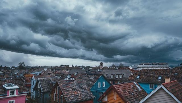 Storm clouds rolling over colorful tiled roofs of rainy townscape with dormers and chimneys