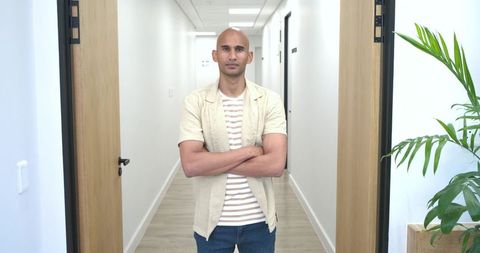 African american man standing with arms crossed in modern office hallway, confident posture