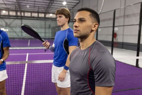 Focused padel team preparing for match on indoor purple court, players in huddle