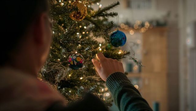 Person Decorating Christmas Tree with Festive Baubles and Lights