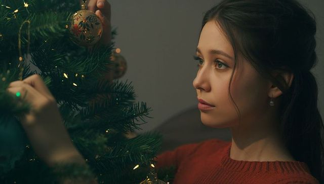 Woman decorating christmas tree with golden ornaments at home