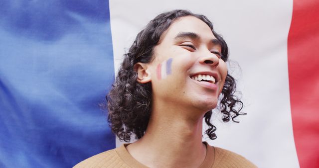 Portrait of happy biracial man with flag of france in background and on cheek. Spending quality time at home.