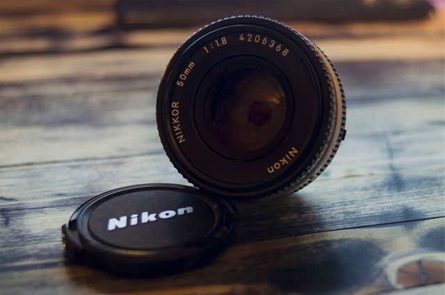 Nikon 50mm lens positioned at an angle on a wooden surface. Lens cap placed next to the lens. Ideal for blogs, articles, or tutorials related to photography, camera gear reviews, photography equipment guides, and photographers' portfolios.