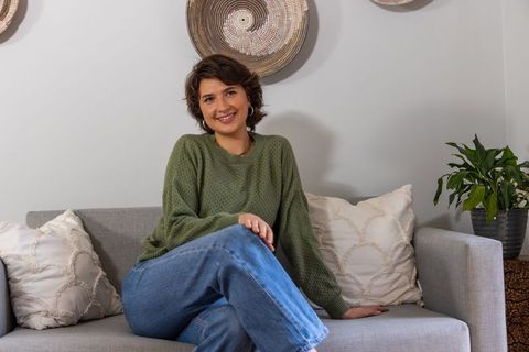 Smiling woman relaxing on sofa in cozy living room with woven baskets and houseplant