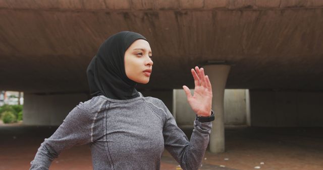 Muslim woman jogging outdoors, wearing a hijab and athletic apparel. Bridge and urban background, highlighting fitness and determination. Suitable for promoting healthy lifestyle, inclusivity, women's fitness programs, and urban exercise routines.