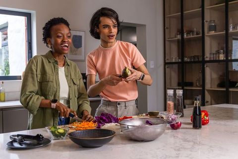 Multicultural friends peeling avocado and chopping vegetables on marble kitchen island