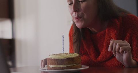 Senior Woman Celebrating Birthday at Home Blowing Candle
