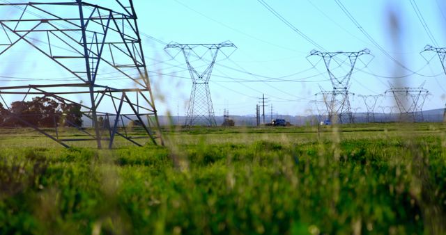 Power transmission towers stretch across a green field under a clear blue sky, with copy space. The electrical infrastructure dominates the landscape, signifying the importance of energy distribution in modern society.
