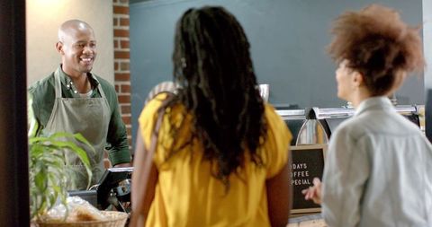 Smiling barista serving customers at coffee counter, espresso machine, pastries on display