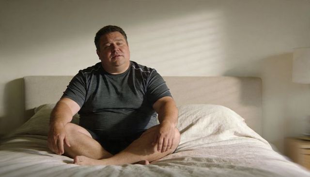 Middle-aged Man Sitting on Bed in Morning Light Contemplating Quiet Solitude