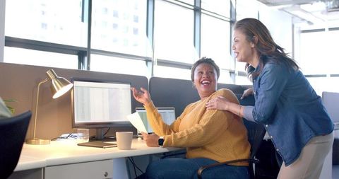 Diverse coworkers collaborating at open office desk, woman pointing at spreadsheet