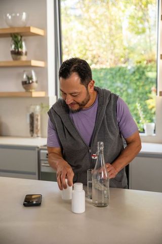 Mature asian man checking prescription pills at kitchen island with water and smartphone