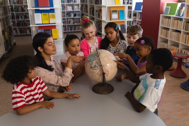 Female teacher explaining globe to a diverse group of children in a school library. Ideal for educational content, school brochures, multicultural learning materials, and geography-related articles.