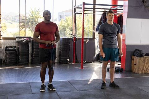 Black and white male training partners standing with jump ropes in sunlit urban gym