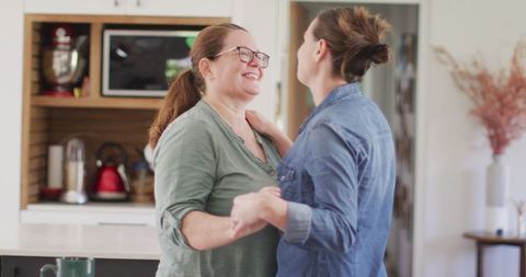 Caucasian Lesbian Couple Smiling and Dancing in Kitchen