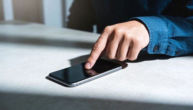 Right Hand Touching Smartphone on Sunlit Minimalist Desk with Blue Shirt Cuff and Shadow