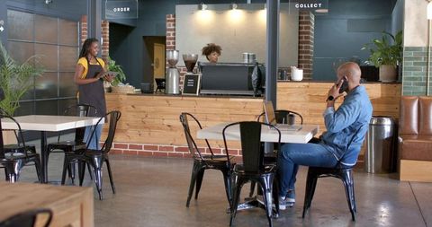 Modern industrial cafe scene with barista, customer on phone and open espresso counter