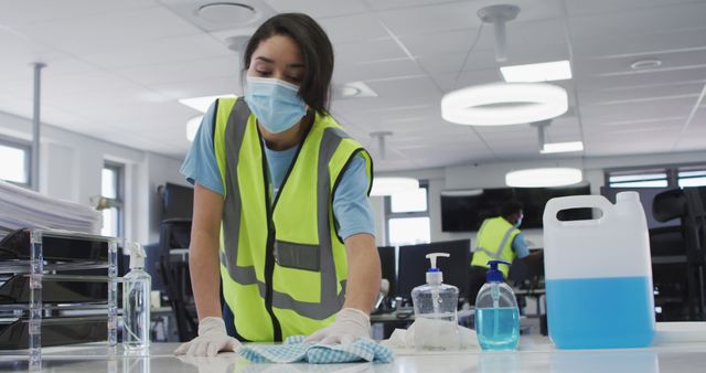 Biracial woman in face mask cleaning countertol and disinfecting office. Office, work, hygiene, health, coronavirus, unaltered.