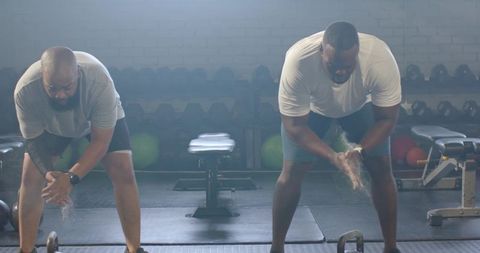 African american men clapping chalk hands preparing kettlebell lifts gym team training