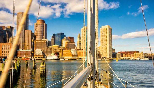 Sailboat foredeck framing city skyline at sunlit marina harbor