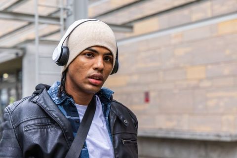 Listening to music at transit shelter, wearing beanie and leather jacket