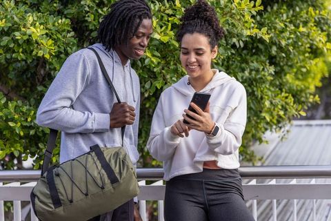 African american duo checking phone and relaxing after outdoor workout by greenery