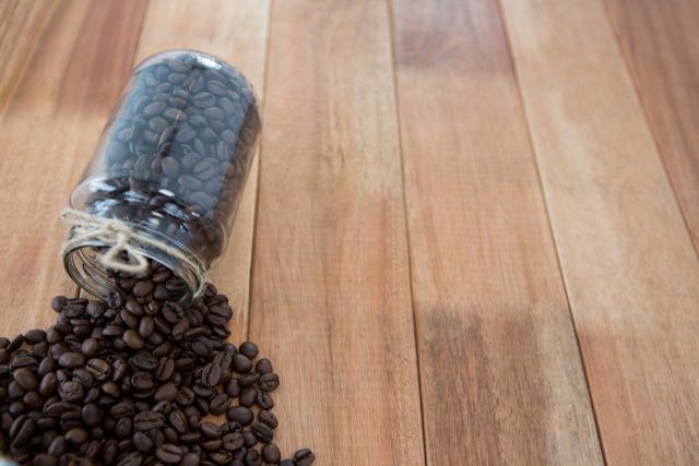 Coffee beans spilling out of jar on wooden table