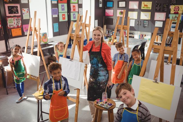 Art teacher standing with a diverse group of children in a drawing class. Children are wearing aprons and standing in front of easels with blank canvases, ready to paint. The classroom is filled with colorful artwork on the walls. Ideal for use in educational materials, school brochures, art class promotions, and articles about creative learning and child development.
