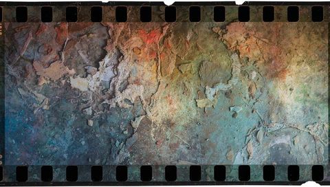 Weathered cracked plaster texture on 35mm film strip with torn edges and teal patina
