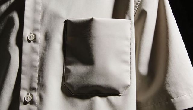Beige short-sleeve shirt close-up featuring patch pocket, buttons, stitching, textured fabric