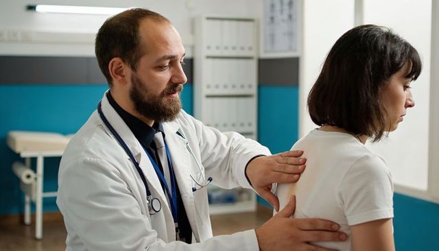 Doctor examining patient upper back during clinical spine and thorax assessment in modern clinic